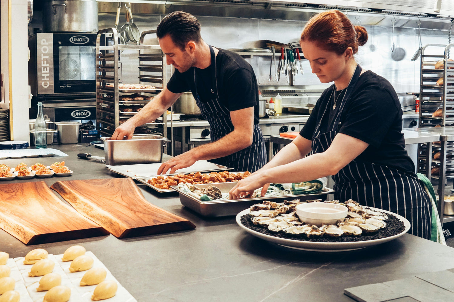 Two chefs preparing food in a kitchen with various cooking equipment.