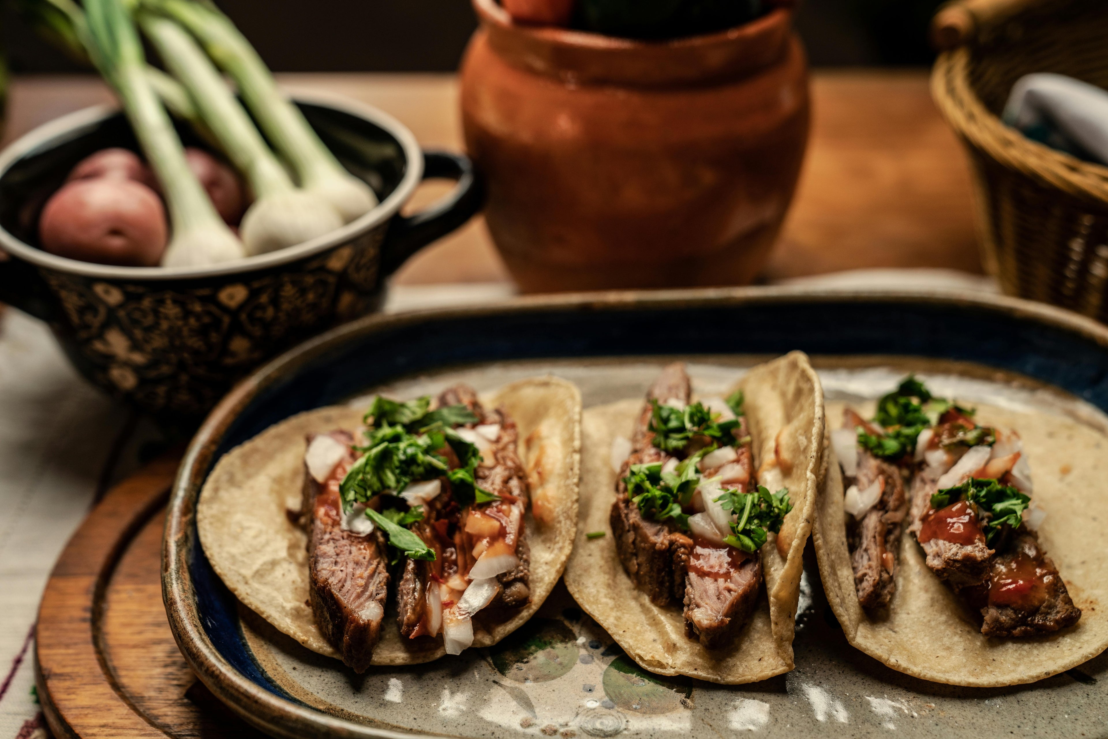 Three tacos with meat and greens on a plate with a rustic background