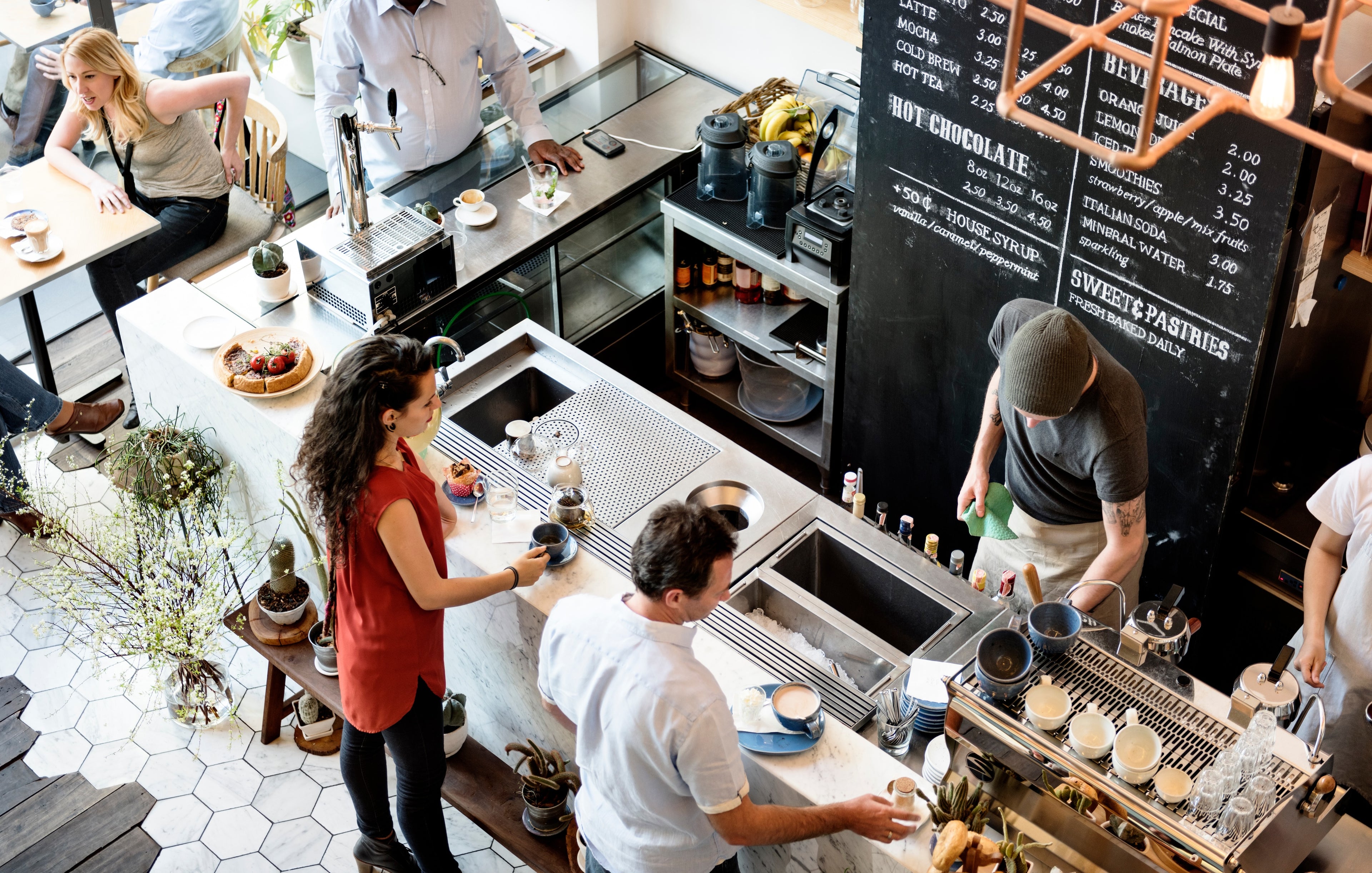 People working in a busy coffee shop with a large chalkboard menu.
